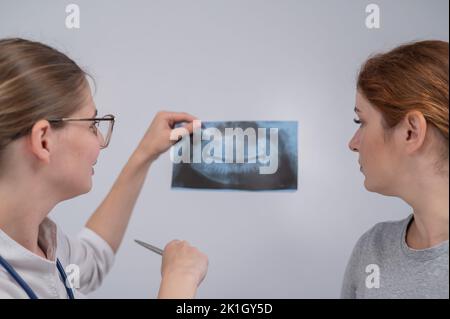 Eine Ärztin und ein Patient an der Rezeption diskutieren über eine Röntgenaufnahme des Kiefers. Stockfoto