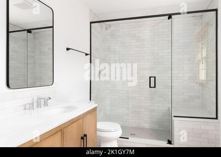 Ein wunderschönes, luxuriöses, modernes Bad mit hellem Holzschrank, bodenebener Dusche mit Marmorwänden mit U-Bahn-Fliesen, schwarzen Wasserhähnen und Hardware. Stockfoto