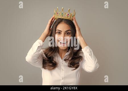 Portrait der Arroganz Frau mit goldener Krone auf dem Kopf, Führung und Erfolg. Attraktive reiche arrogante Mädchen tragen Krone isoliert über grau Stockfoto