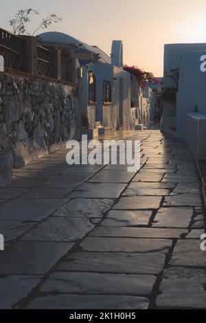 Goldenes Sonnenaufgangslicht über einer Kopfsteinpflasterstraße der Altstadt während eines ruhigen Morgens im griechischen Inseldorf Oia, Santorini, Griechenland. Stockfoto