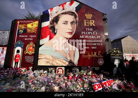 Nach dem Tod des britischen Monarchen legt man Blumen auf ein Wandgemälde, das Königin Elizabeth II. Auf der Shankill Road in Belfast darstellt. Stockfoto