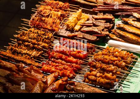 Muscheln, Tintenfische, Fische, Garnelen und viele andere geräucherte und getrocknete Meeresfrüchte auf der Markttheke. Fleisch auf Spiessen, Stöcken Stockfoto