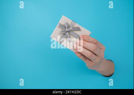 Die Hand einer Frau ragt aus einem blauen Papierhintergrund und einer Geschenkbox. Stockfoto