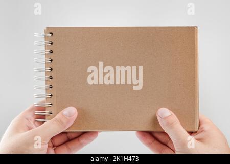 Notizblock in der Hand. Leerer Notizblock in den Händen eines Mannes auf weißem Hintergrund. Hände halten ein Buch ohne Text. Ein Mann hält ein Buch mit leerem Cover Stockfoto