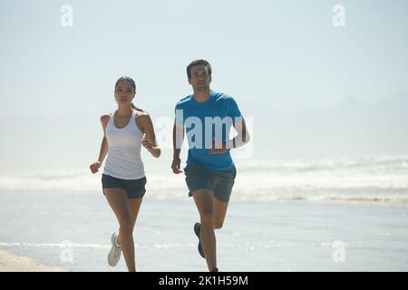 Sie sind auf lange Sicht darin. Ein junges Paar joggt zusammen am Strand. Stockfoto