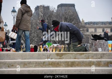 Ein Straßenhändler verkauft Miniatur-Eiffelturm auf dem Bürgersteig vor dem echten Eiffelturm in Paris Stockfoto