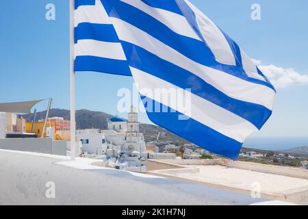 Die blau-weiße griechische Flagge schwingt über dem Quanit, dem traditionellen Dorf Pyrgos Kallistis und der orthodoxen Heiligen Kirche der Verklärung des Th Stockfoto