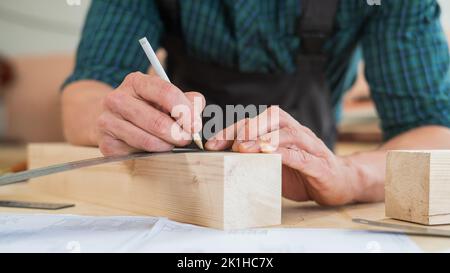 Ein Zimmermann mißt Holzbohlen und macht in einer Werkstatt mit einem Bleistift Markierungen. Stockfoto