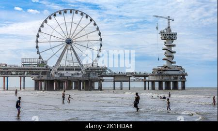 Das Riesenrad und der Piertoren am Pier von Scheveningse, wo Menschen am Strand an der Küste schwimmen und spielen Stockfoto