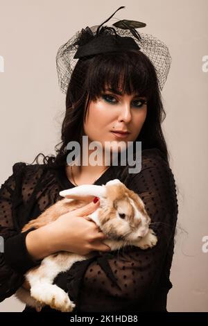 Eine junge Frau in dunklen Kleidern hält ein faltes Kaninchen in den Ruken Stockfoto