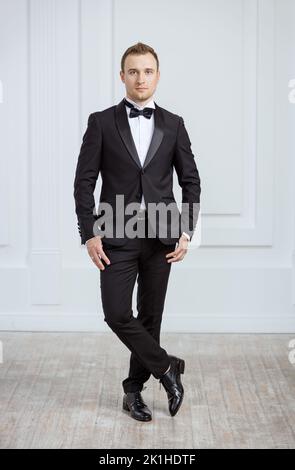 Attraktiver junger Mann, der im Smoking drinnen steht und die Kamera anschaut Stockfoto