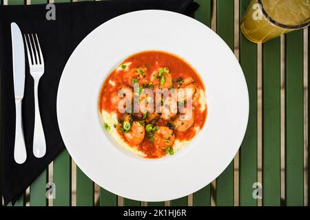 Gegrillte Garnelen gepaart mit Grütze, garniert mit Koriander und einer roten Sauce, gepaart mit Gabel und Messer mit schwarzer Serviette Stockfoto