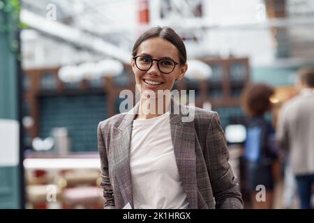 Porträt einer lächelnden Geschäftsfrau, die im modernen Büro auf dem Hintergrund ihrer Kollegen steht Stockfoto