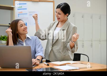 Zwei glückliche und fröhliche, tausendjährige asiatische Geschäftsfrauen feiern gemeinsam im Büro ihren Projekterfolg. Gute Nachrichten erhalten, Projekt gewinnen. Stockfoto