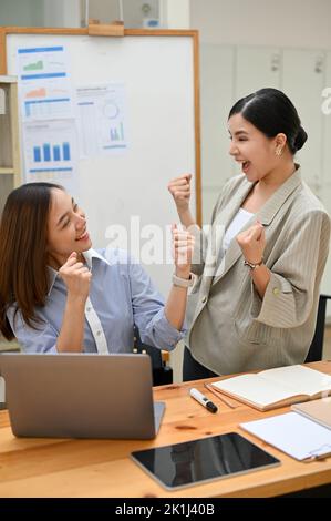 Portrait, zwei glückliche und überglückliche Millennial-Asiaten-Geschäftsfrauen feiern gemeinsam im Büro ihren Erfolg. Siegreich, Zielerreichung toge Stockfoto