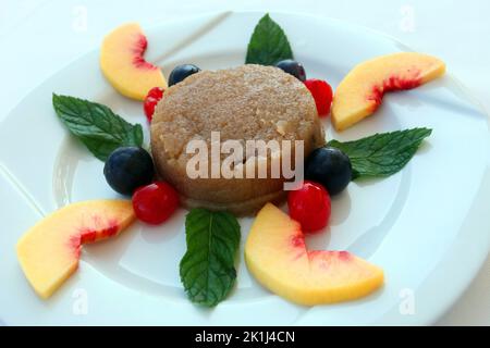 Traditionelles türkisches Dessertgrieß Halva (türkisch: Irmik helvasi) mit Pfirsich auf dem Dessertteller. Stockfoto