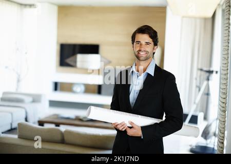 Hes begeistert sich für seine Pläne. Ein hübscher junger Architekt, der einen Anzug trägt und einige Designpläne hält. Stockfoto