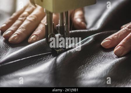 Die Hände der Frauen beim Nähen auf professionelle Ausrüstung. Nähen von Leder in der Produktion. Nahaufnahme. Stockfoto