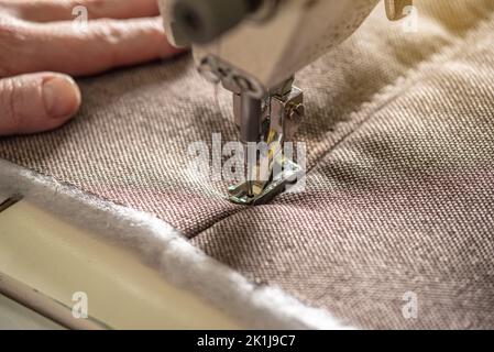 Die Hände der Frauen beim Nähen auf professionelle Ausrüstung. Nähgewebe in der Produktion. Nahaufnahme. Stockfoto