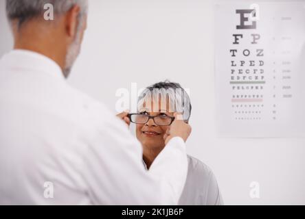 Ein neues Augenpaar. Ein Optiker, der eine Brille auf einen Patienten legt. Stockfoto