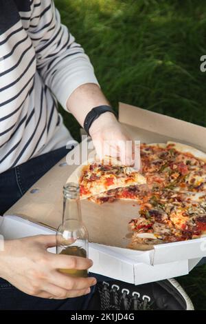 Ein junger Mann, der bei einem Picknick Pizza isst. Stockfoto