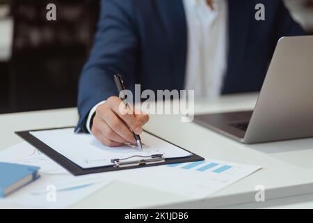 Nahaufnahme der Hand eines Geschäftsmannes, der sich während der Arbeit am Laptop im Büro Notizen machte Stockfoto