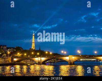 Paris, Frankreich - 19. April 2022: Beleuchteter Eiffelturm und Pont des Invalides, von der seine aus gesehen bei Nacht Stockfoto