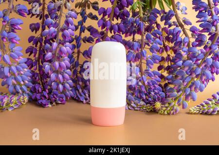 Mockup weiße Tube Flasche mit rosa Schraubverschluss für die Hautpflege kosmetische Sommer Sonnencreme und blau lila Lupinenblüten auf braungoldenen Hintergrund. Produk Stockfoto