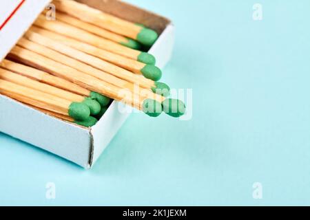 Viele Streichhölzer mit grünen Köpfen in einer Streichholzschachtel auf blauem Hintergrund mit Kopierraum Stockfoto