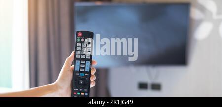 Hand mit Fernbedienung für Smart TV im modernen Zimmer zu Hause oder in einem Luxushotel einstellen Stockfoto