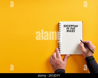 Männliche Hand schreiben Ausnahme zu den Regeln auf einem Notizblock. Ausschluss von Regeln, Richtlinien oder Regelungskonzepten. Stockfoto