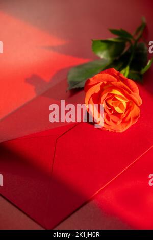 Schöne rote Rosen Blumen in postalischem roten Umschlag auf rotem Hintergrund, Kopierraum für Text, Frühling, Grußkarte für Urlaub. Blumenlieferung. Zarte rote gelbe Rosen. Monochrome Minimal trendige Komposition. Romantische Blumen Stockfoto