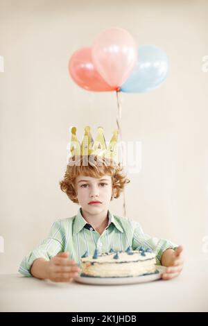 Der König verlangt Ihre Anwesenheit. Ein niedlicher kleiner Junge, der ernst aussieht, während er mit seinem Geburtstagskuchen an einem Tisch sitzt. Stockfoto