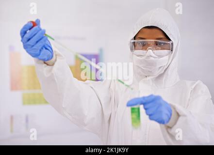 Clever und sorgfältig arbeiten. Eine junge Wissenschaftlerin in Schutzkleidung, die in ihrem Labor eine Pipette verwendet. Stockfoto