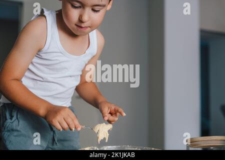 Kaukasischer Junge gießt Teig mit Löffel in die Form für Muffins, die Zeit in die Küche verbringen. Glückliche Familie in der Küche. Kekse backen Stockfoto