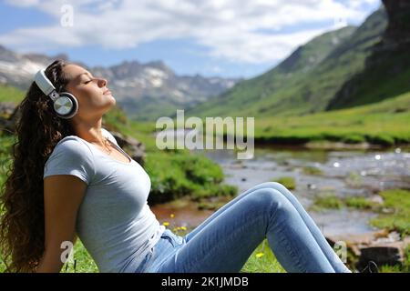 Seitenansicht Porträt einer Frau, die sich entspannt und Musik mit Kopfhörern in der Natur hört Stockfoto