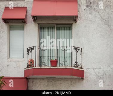 Schönes altes Haus mit Fenstern und Balkon mit Blumentöpfen. Weiße Hausfassade mit roten Türen und Fenstern. Niemand, Blick auf die Straße, Reisefoto Stockfoto