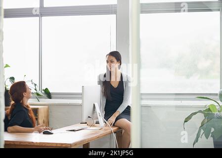 Schnelles Gespräch zwischen Kollegen. Zwei Geschäftsfrauen führen ein freundliches Gespräch am Schreibtisch. Stockfoto