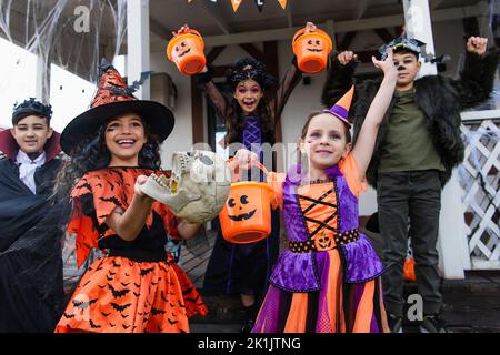 Aufgeregt multikulturelle Freunde in halloween-Kostümen halten Trick or Treat Eimer in der Nähe des Hauses Stockfoto