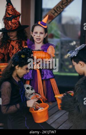 Präteen Mädchen hält halloween Kürbis in der Nähe von multiethnischen Kindern mit Eimern im Freien Stockfoto