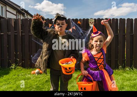 Multiethnische Kinder in halloween-Kostümen halten Eimer und Grimacing an der Kamera im Hinterhof Stockfoto