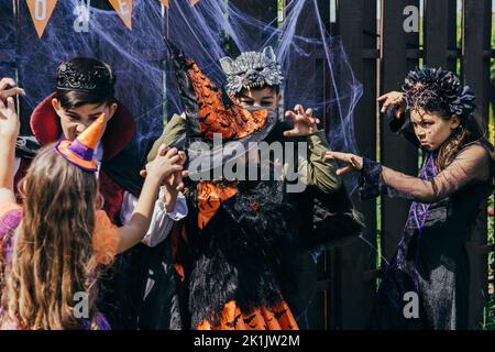 Multiethnische Kinder in festlichen Kostümen erschrecken sich gegenseitig während der halloween-Party im Hinterhof Stockfoto