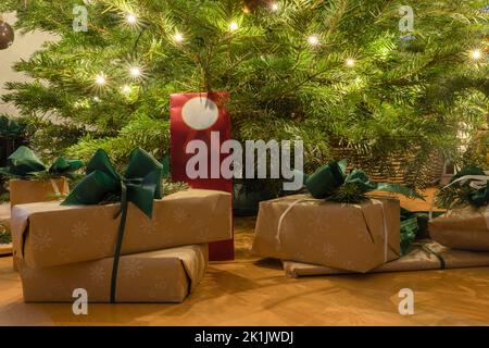 Wunderschön gewickelte Geschenke mit Schleifen unter dem Weihnachtsbaum mit Lichtsternen Stockfoto