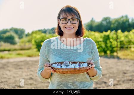 Frau mit Knoblauch Ernte in Weidenschale, Gemüsegarten im Freien Stockfoto