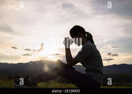 Silhouette einer christlichen Frau, die bei Sonnenuntergang betet. Christliche Religion Konzept Hintergrund. Hände im Gebet. Verehren sie gott mit Religion Konzept. Stockfoto