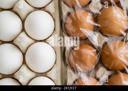 Draufsicht auf weiße und braune Hühnereier in Tabletts mit Zellophan Stockfoto