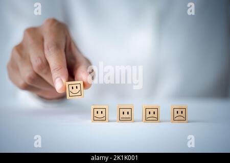 Kundendienst- und Zufriedenheitskonzept, Kundenhand wählen Smiley Face Icon auf Holzwürfel, Service Rating, Zufriedenheitskonzept. Stockfoto