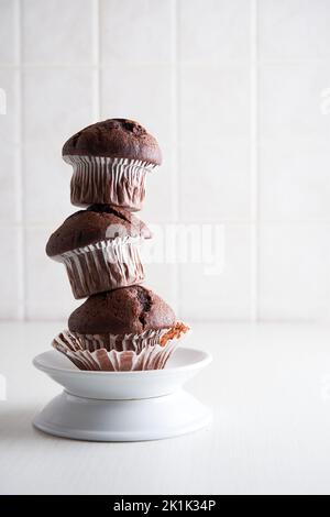 Stapel von hausgemachten Schokoladen-Muffins in Pappbechern auf einem Teller im Küchenhintergrund. Nahaufnahme. Speicherplatz kopieren. Frühstück Biskuitkuchen Stockfoto