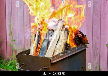 Brennende Kiefernstämme für Kohlen. Starke Flamme auf dem Grill. Brennendes Feuerholz auf dem Grill. Das Feuer brennt auf dem Grill. Stockfoto