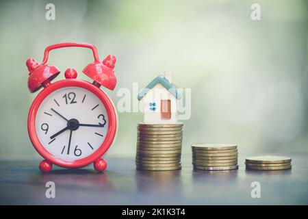 Stapel von Geldmünzen Aufwachsen mit Haus-Modell und Wecker-Konzept im Geschäft über Darlehen verkaufsfinanzierung Hypothek und den Kauf von zu Hause, Vintage Ton. Stockfoto